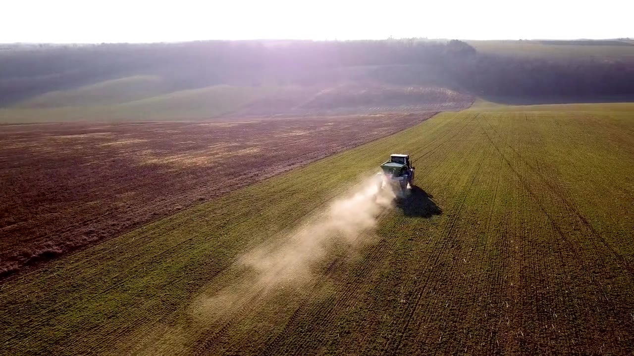 Traktor bei der Feldarbeit im Morgenlicht auf hügeligem Grünland