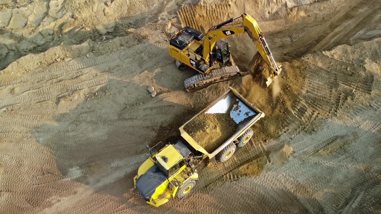 Kettenbagger belädt einen knickgelenkten Dumper — Luftaufnahme der Baustelle